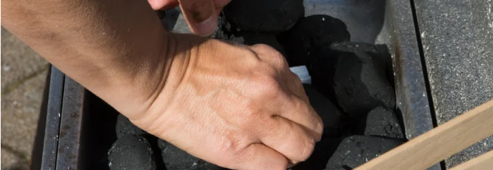 Person legt Anzündwürfel auf Holzkohle